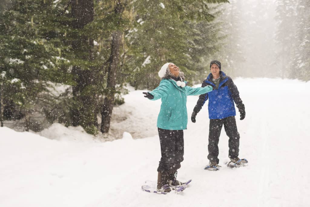 Smiling ethnic senior couple snowshoeing in the forest